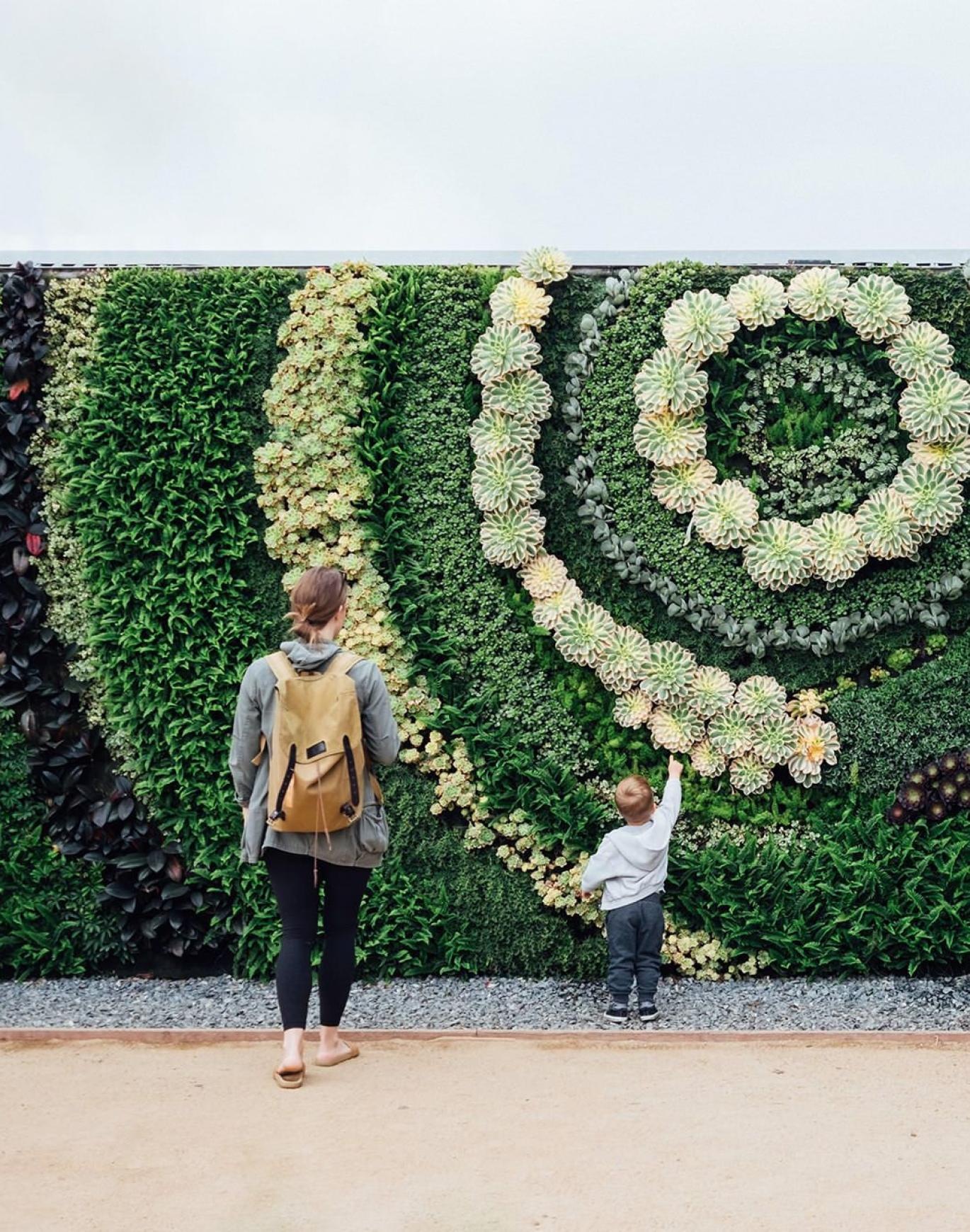 mother and child standing in front of a mural made of plants